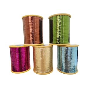 May include: Six spools of metallic thread in shades of copper, green, gold, pink, and blue. The thread is wound on wooden spools with yellow rims. The spools are arranged in a visually appealing stack, showcasing the range of colours.