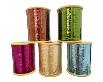 Puede incluir: Seis carretes de hilo metálico en varios colores, incluyendo cobre, verde, dorado, rosa y azul. El hilo está enrollado en carretes de madera con bordes amarillos. Los carretes están apilados en una disposición visualmente atractiva.