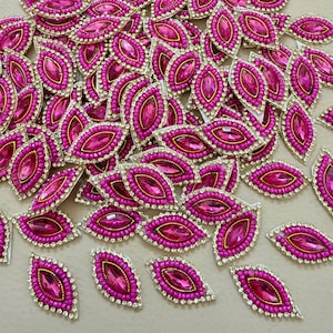 Puede incluir: Un conjunto de adornos rosas en forma de hoja. Cada pieza presenta una gema rosa central facetada, un borde dorado, pequeñas cuentas rosas y un borde plateado. Estos elementos decorativos son ideales para manualidades y añadir brillo.