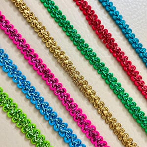 May include: Close-up of colorful decorative trim in various colors, including green, gold, pink, red, and blue. The trim has a scalloped edge and a glittery finish, suitable for crafts and embellishments.