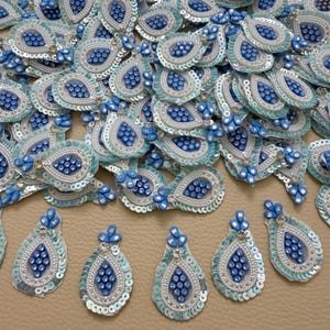 May include: A collection of teardrop-shaped embroidered patches featuring a central cluster of blue beads surrounded by white seed beads and light blue sequins. Each patch has a pointed top with three blue beads and a clear rhinestone accent.