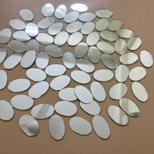 May include: A scattering of small, oval-shaped mirror pieces. The mirrors reflect light, creating a bright and shiny appearance. These decorative mirrors are suitable for craft projects or home decor, reflecting light.