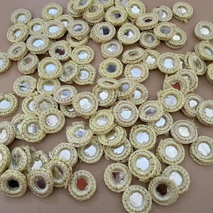 Könnte beinhalten: Eine Sammlung kleiner, runder Zierspiegel mit einem gewebten, beigefarbenen Rand. Die Spiegel haben eine reflektierende Oberfläche und sind über das Bild verstreut. Diese Bastelmaterialien sind ideal zum Verschönern von Kleidung oder Accessoires.