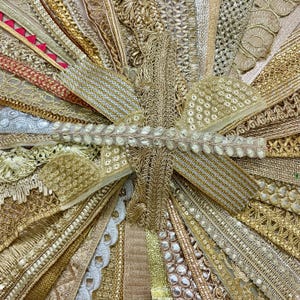 May include: A collection of gold and silver decorative trims, ribbons, and lace. The image displays a variety of textures, patterns, and widths, with metallic threads and embellishments. The trims are arranged in a radial pattern, showcasing the variety of designs.