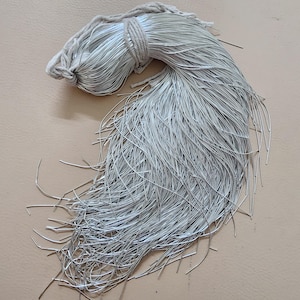 Op de afbeelding: Een bundel zilverkleurige draad, stevig gebonden met een natuurlijk gekleurd koord aan één uiteinde. De draadstrengen waaieren uit en creëren een textuurrijke, vloeiende uitstraling. De draad wordt waarschijnlijk gebruikt voor knutselen of het maken van sieraden.