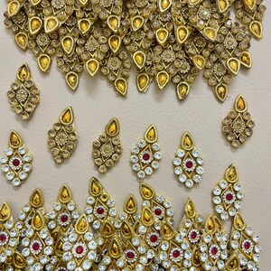 Peut inclure: Un ensemble de bijoux doré orné d'un collier et de plusieurs paires de boucles d'oreilles. Les pièces sont ornées de pierres précieuses claires, rouges et ambrées. Les boucles d'oreilles sont en forme de goutte d'eau et le collier a un design détaillé et superposé.