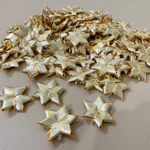 May include: A pile of gold and silver star-shaped embellishments. The stars have a woven texture with gold edging. Some are scattered, others piled together. These could be used for crafts or decorative purposes.