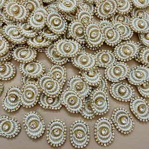Op de afbeelding: Een verzameling ovale versieringen met een centrale strass-steen, omringd door concentrische cirkels van witte parels. De randen zijn afgewerkt met goudkleurig metaal en kleine strass-steentjes. Deze decoratieve elementen zijn geschikt voor diverse knutselprojecten.