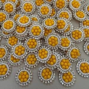 May include: A selection of yellow beaded embellishments. Each has a central cluster of yellow beads, encircled by white faux pearls and a border of clear rhinestones. Suitable for various craft projects.