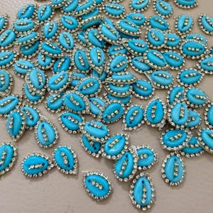 Può includere: Una collezione di abbellimenti ovali color turchese. Ogni pezzo presenta un bordo dorato con strass trasparenti e un design centrale di tre barre dorate. Questi elementi decorativi sono ideali per l'artigianato e la creazione di gioielli.