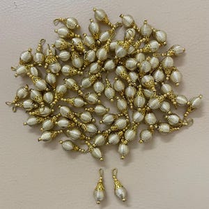 May include: A collection of silver and gold-toned decorative beads. Each bead has a spiral design with gold filigree accents and a loop for stringing. The beads are scattered on a neutral surface, with two beads isolated at the bottom.