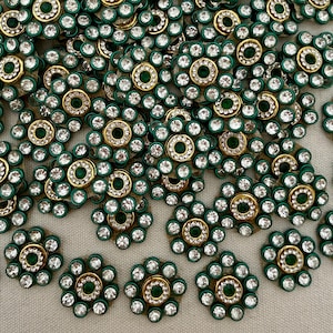 Könnte beinhalten: Eine Ansammlung kreisförmiger blumenförmiger Verzierungen mit einem zentralen dunkelgrünen Stein, umgeben von einem Ring aus klaren weißen Strasssteinen, eingefasst in einen goldfarbenen Metallrahmen mit dunkelgrünem Rand.