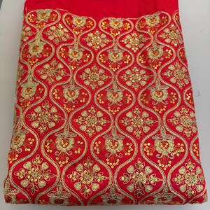 May include: A vibrant red fabric featuring an intricate gold embroidered pattern of repeating ogee shapes. Each section contains a detailed floral motif accented with small, shimmering gold sequins stitched throughout the design.