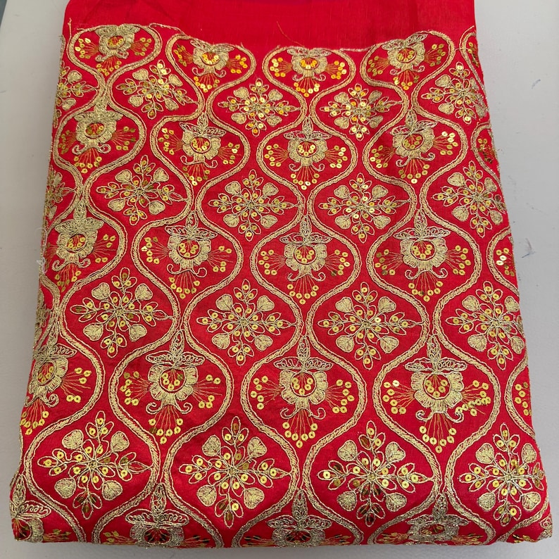 May include: A vibrant red fabric featuring an intricate gold embroidered pattern of repeating ogee shapes. Each section contains a detailed floral motif accented with small, shimmering gold sequins stitched throughout the design.