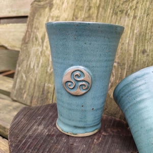 Könnte beinhalten: Zwei blaue Keramikbecher mit einem keltischen Knotendesign. Die Becher sind handgefertigt und haben ein rustikales, erdiges Aussehen.