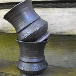 Peut inclure: Deux pots en céramique noire avec un motif décoratif. Les pots sont empilés l'un sur l'autre.