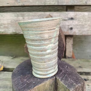 Könnte beinhalten: Eine kleine, weiße Keramikvase mit einem strukturierten, gestreiften Design. Die Vase steht auf einer Holzoberfläche.