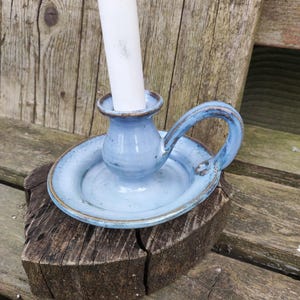 Può includere: Una tazza di ceramica bianca con manico nero e la scritta "But First, Coffee" in nero, con un carattere a mano. La tazza è su una superficie bianca.