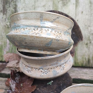 Puede incluir: Dos cuencos de cerámica apilados con un esmalte marrón claro y un esmalte azul verdoso. Los cuencos tienen un patrón decorativo de pequeñas flores alrededor del borde.