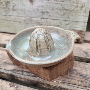 May include: A ceramic lime squeezer with a light green glaze and a textured surface. The squeezer is sitting on a wooden surface.