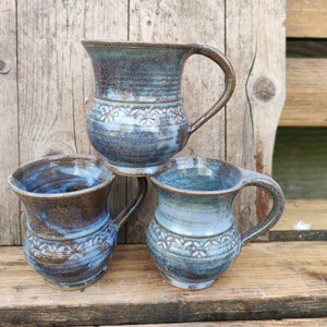 Może przedstawiać: Trzy ceramiczne kubki w kolorze niebieskim i brązowym z ozdobnym wzorem. Kubki mają uchwyty i są ułożone jeden na drugim.