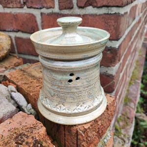 Può includere: Un set di tre tazze in ceramica con finitura opaca e macchiettata. Le tazze sono nei toni del crema, grigio chiaro e grigio scuro. Ogni tazza ha un design semplice e minimalista.