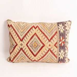 Peut inclure: Un coussin rectangulaire présentant un motif géométrique tissé dans des tons de rouge, jaune et beige. Le design comprend de grands losanges centraux et un panneau latéral vertical avec des motifs en forme d'étoile gris foncé, rouge et crème.