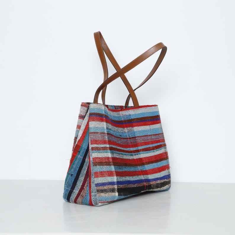May include: A striped tote bag with brown leather straps. The bag is made of a woven fabric with red, blue, and white stripes.