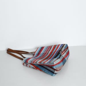 May include: A striped tote bag with brown leather straps. The bag is made of a woven fabric with red, blue, and white stripes.