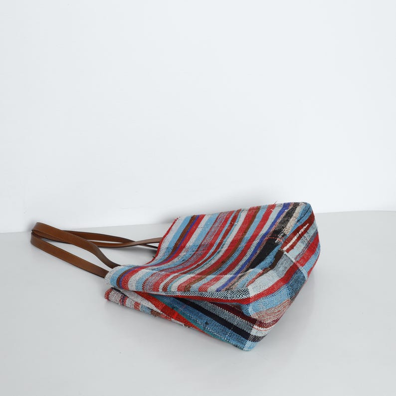 May include: A striped tote bag with brown leather straps. The bag is made of a woven fabric with red, blue, and white stripes.