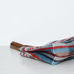 May include: A colorful striped tote bag with a brown leather handle. The bag is made of woven fabric and has a blue, red, and white pattern.