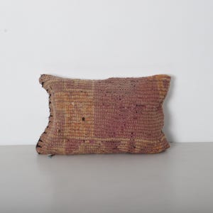 Peut inclure: Coussin rectangulaire décoratif avec une texture tissée. Le coussin présente un motif patchwork dans des tons de rose, beige et marron. Les bords sont finis avec une bordure plus foncée, peut-être noire. Pour la décoration intérieure.