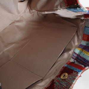 May include: The inside of a woven tote bag with a beige lining and a small pocket. The bag is made of colorful stripes in red, blue, green, and yellow.