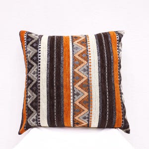 Peut inclure: Un coussin décoratif avec un motif géométrique dans des tons d'orange, de brun et de blanc.