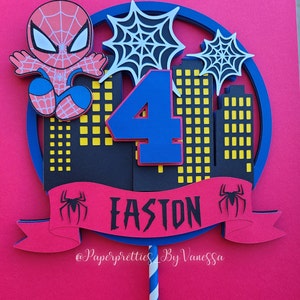 May include: A red and blue Spiderman cake topper with a number 4, a banner that says "Easton", and a cityscape in the background. The topper is on a stick with blue and white stripes.