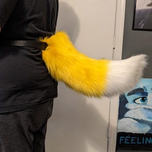 May include: A yellow and white fluffy tail with a black belt attached to the base of the tail.