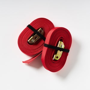 Puede incluir: Dos correas de trinquete rojas con hebillas met&aacute;licas. Las correas est&aacute;n hechas de nylon tejido y tienen una banda el&aacute;stica negra alrededor de cada hebilla.