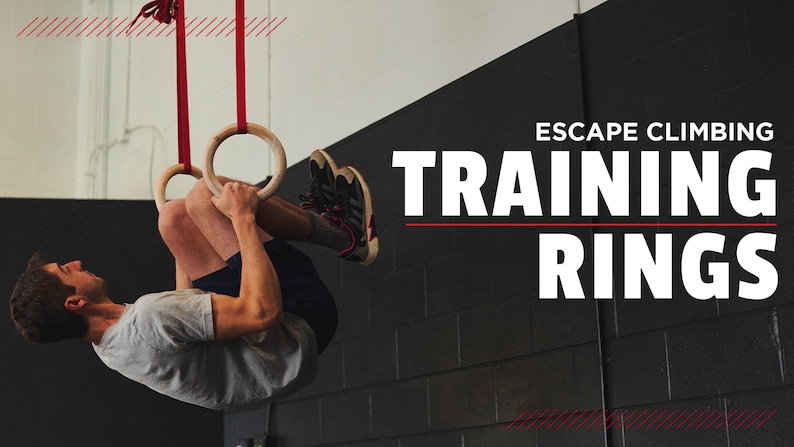Puede incluir: Una persona haciendo un ejercicio de dominadas en anillos de gimnasia de madera colgados de correas rojas. Los anillos est&aacute;n suspendidos de un techo en un gimnasio. El texto "ESCAPE CLIMBING TRAINING RINGS" se muestra en letras blancas sobre una pared de ladrillo negro.