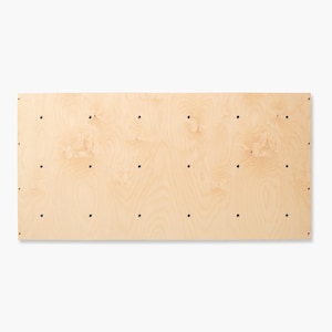 Pode incluir: Um painel retangular de madeira clara com um padrão natural de grão de madeira. O painel tem vários pequenos orifícios de cor escura espaçados uniformemente. A madeira tem uma aparência lisa e inacabada. O painel é provavelmente para um projeto de mobiliário.