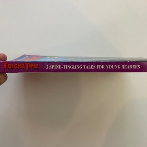 以下が含まれることがあります： 「フライトタイム」というタイトルの紫色のペーパーバック。背表紙には「3 Spine-Tingling Tales for Young Readers」と「Baronet Books」の文字が書かれている。