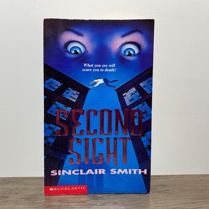 May include: A paperback book titled Second Sight by Sinclair Smith with a blue cover featuring a large pair of eyes at the top, a person falling between two dark buildings, and the text What you see will scare you to death! in white font.