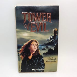 May include: A paperback book titled "Tower of Evil" with a woman on the cover. The title is in large, metallic-looking letters. The cover art features a woman in a black jacket, a castle, and a dark, cloudy sky.