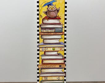 May include: A rectangular bookmark featuring a stack of books with an owl wearing a graduation cap. The books have titles like "History" and "Geography." The bookmark has a yellow background and a black and white checkered border.
