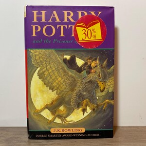 May include: A hardcover book titled "Harry Potter and the Prisoner of Azkaban" with a purple cover and a 30% off sticker. The cover art features a griffin carrying three figures in front of a full moon.