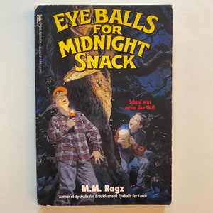 May include: A book cover with a dark green background and a large tree trunk. The title is "Eyeballs for Midnight Snack" in yellow letters. The author is M.M. Ragz. The text "School was never like this!" is in red letters. The cover features two children with flashlights in a dark forest.