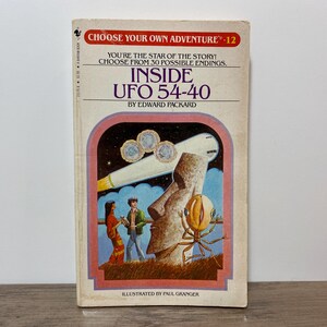 Peut inclure: Un livre de poche vintage intitulé "Inside UFO 54-40" de la série "Choose Your Own Adventure". La couverture présente une illustration d'un OVNI, d'un extraterrestre et de deux personnages. Le livre est d'Edward Packard et illustré par Paul Granger.