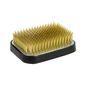 May include: A rectangular flower frog with a black base and numerous gold-colored pins. The pins are closely spaced and arranged to hold flower stems in place for floral arrangements. The frog is designed for stability and ease of use.
