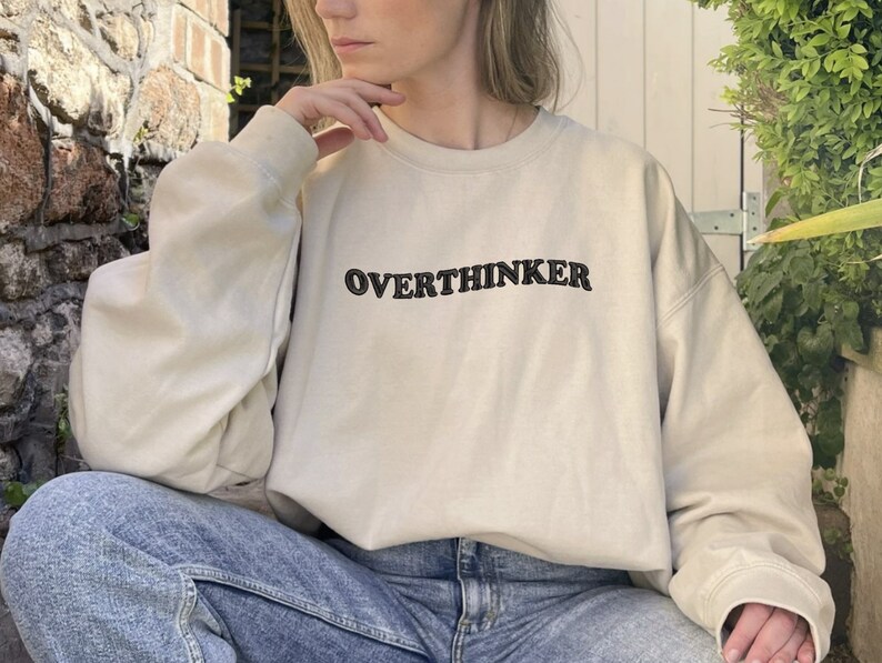May include: A beige sweatshirt with the text "OVERTHINKER" embroidered in black on the front.