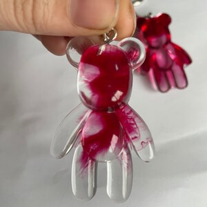 Pode incluir: Um chaveiro de urso de peluche de resina transparente com um design de redemoinho rosa e branco.