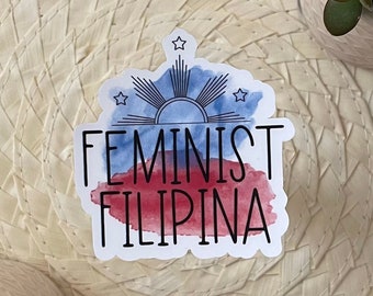 May include: A sticker with a watercolor design of the Philippine flag. The sticker says "Feminist Filipina" in black text.